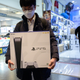 A man holds a PS5 box in a retail store, walking away from other Playstation merchandise on a counter.